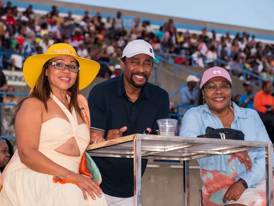 Three guests smile at a table in the stands at the Caribana King and Queen Show, with a full crowd behind them